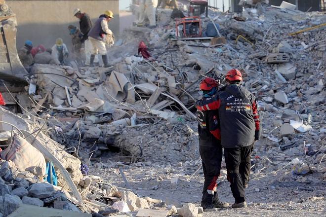 Members of the Zeytinburnu Municipality Search and Rescue Team (ZAK) confort themselves by the rubble of collapsed buildings in Nurdagi, near Gaziantep, on February 13, 2023. Two men holding each other, wearing work clothes, surrounded by rubble.