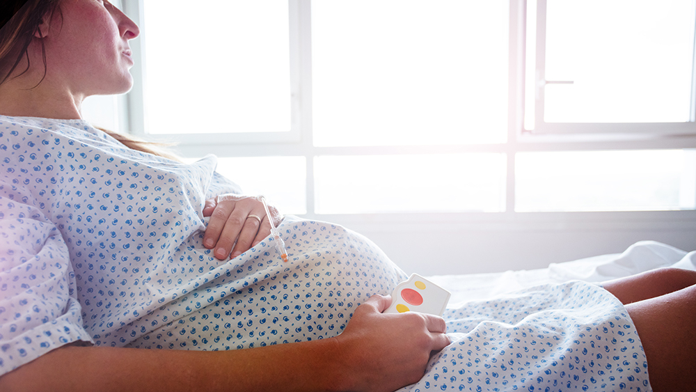 Pregnant woman resting in hospital bed, clutching stomach, worried look.