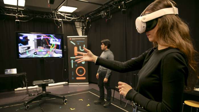 Woman in foreground with XR headset moving her hands. Pedro and screen in background.