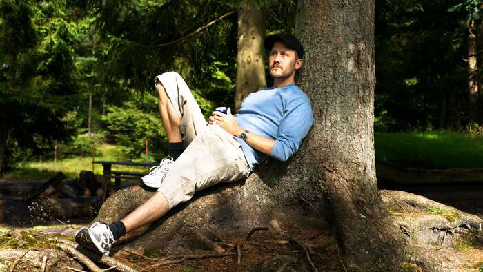 Image of a Norwegian man sitting by a tree in the woods