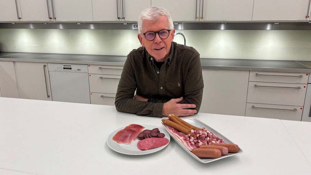 Image shows a man with glasses in front of plates with bacon, salami and other processed meat