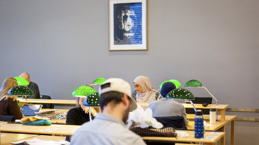 Flere studenter sitter på lesesalen med hver sin PC og ser konsentrerte ute. 
