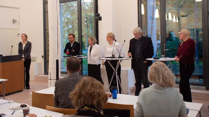 Bilde av deltakerne i panelet som står oppreist på scenen. På siden står studiedekanen. 