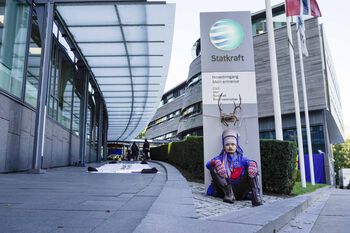 På bildet demonstrerer aksjonist Mihkkal Hætta utenfor Statkraft i anledning to-årsmarkeringen for dommen. Personen sitter nede på bakken foran hovedinngangen til Statkraft