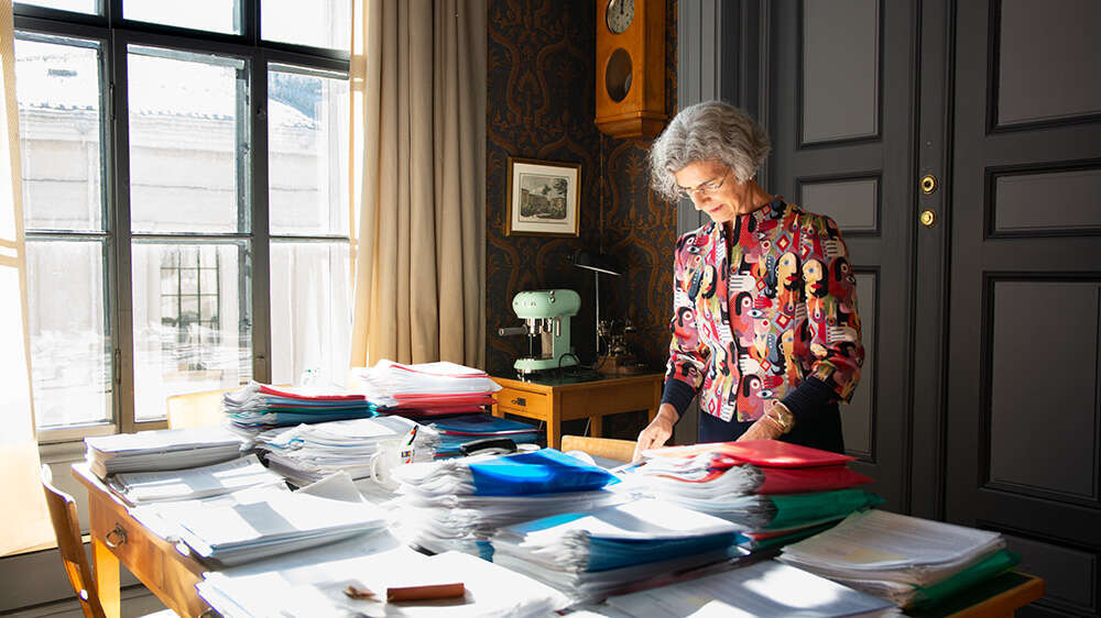 Fotografi av Giuditta på et kontor, hun har masse dokumeter på en pult foran seg.