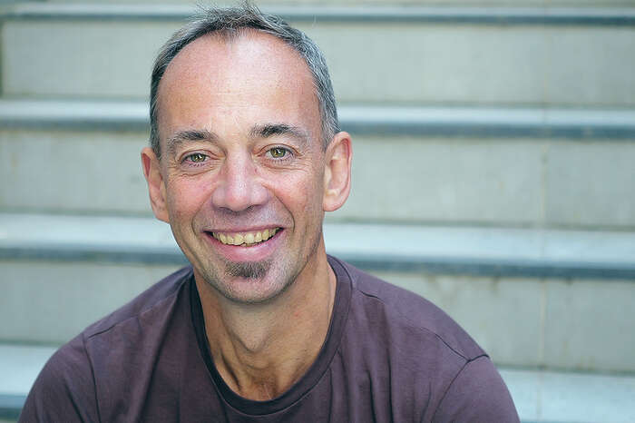 Portrettbilde av jusprofessor og innovasjonsvinner Malcolm Langford. Han sitter i en trapp og smiller, med en lilla t-skjorte. 