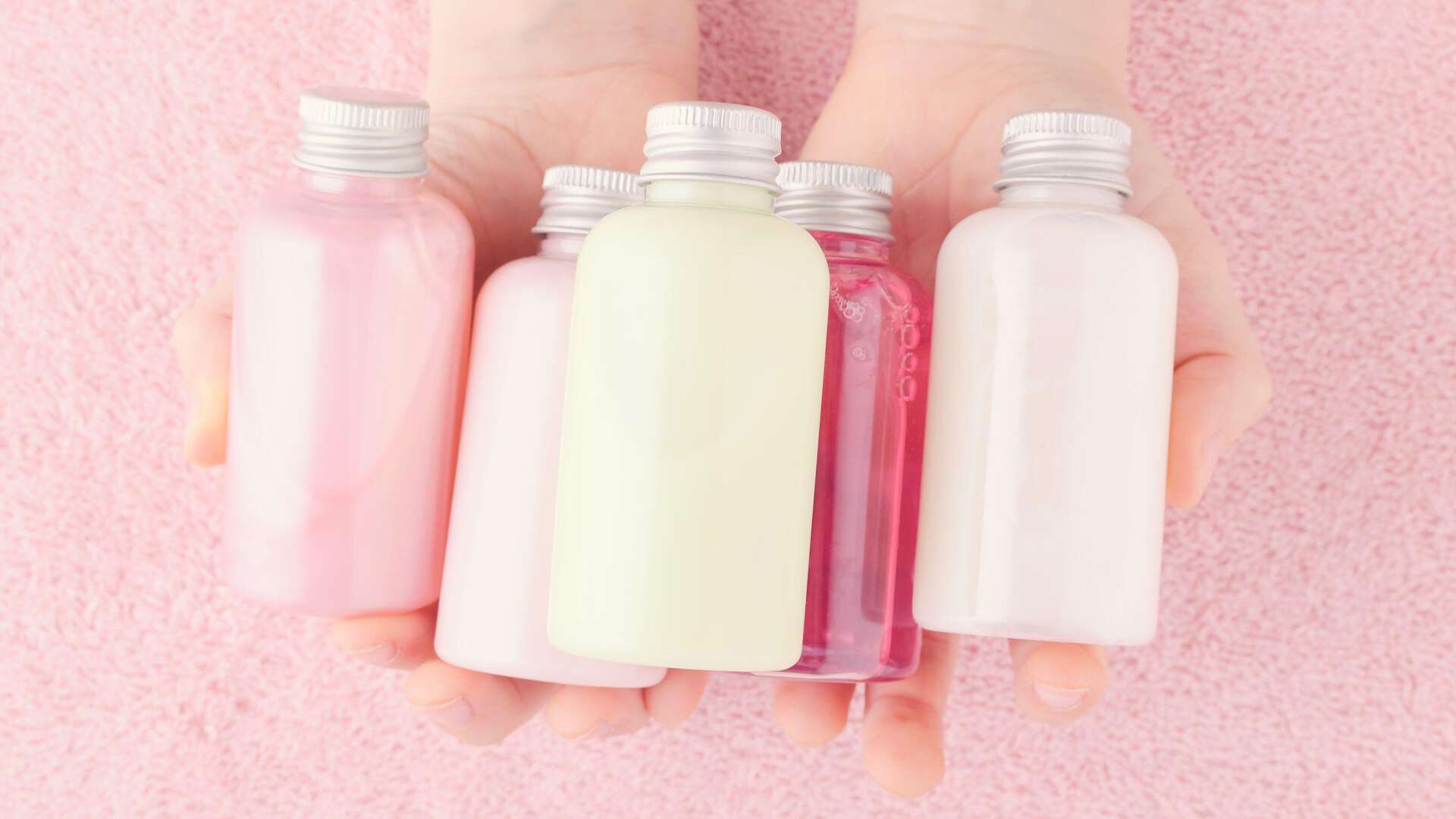 Bilde av fem flasker med hårprodukter som ligger i hånden til en person