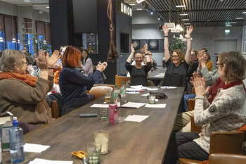 Fotografi av en gruppe med kvinner rundt et bord, som feirer at de har vunnet på quiz. De klapper og har hendene i været.