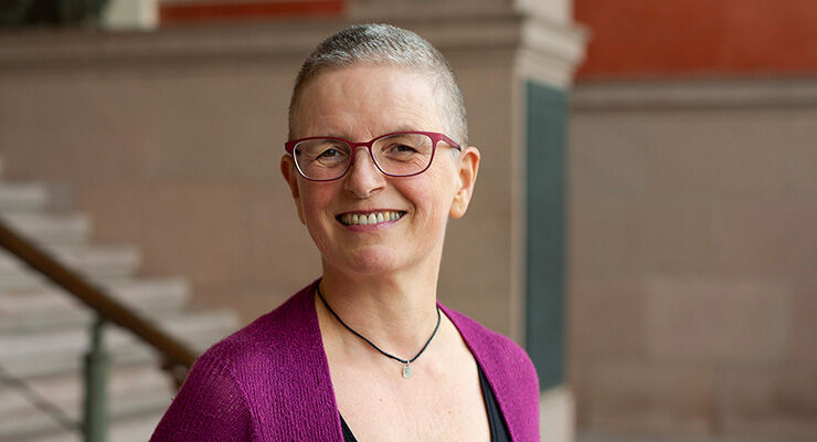 Kvinnelig professor smiler til kamera utenfor universitetsbygg.