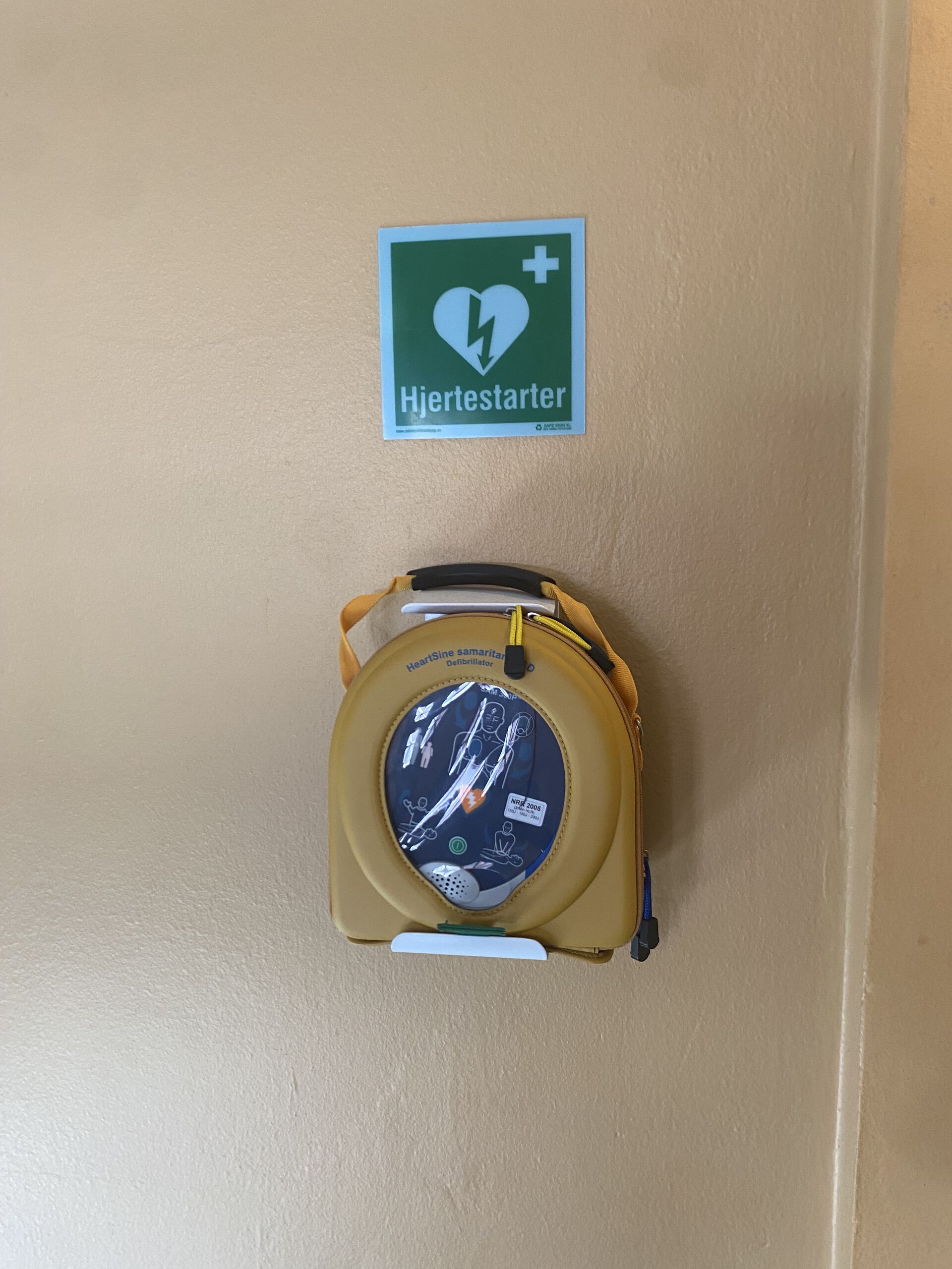 Hjertstarter som henger på en gul vegg.