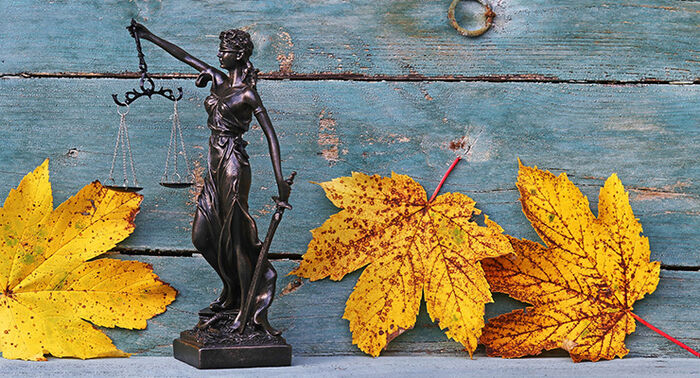 Statue av Justitia med løvblader foran blått treverk.