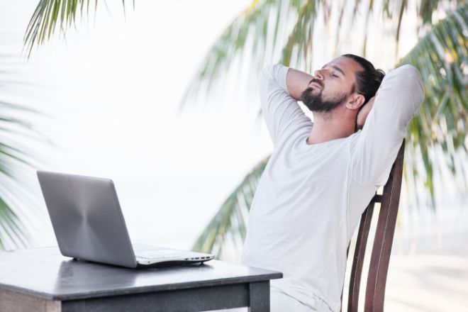Mann sitter ute og nyter solen med PC på et bord. 