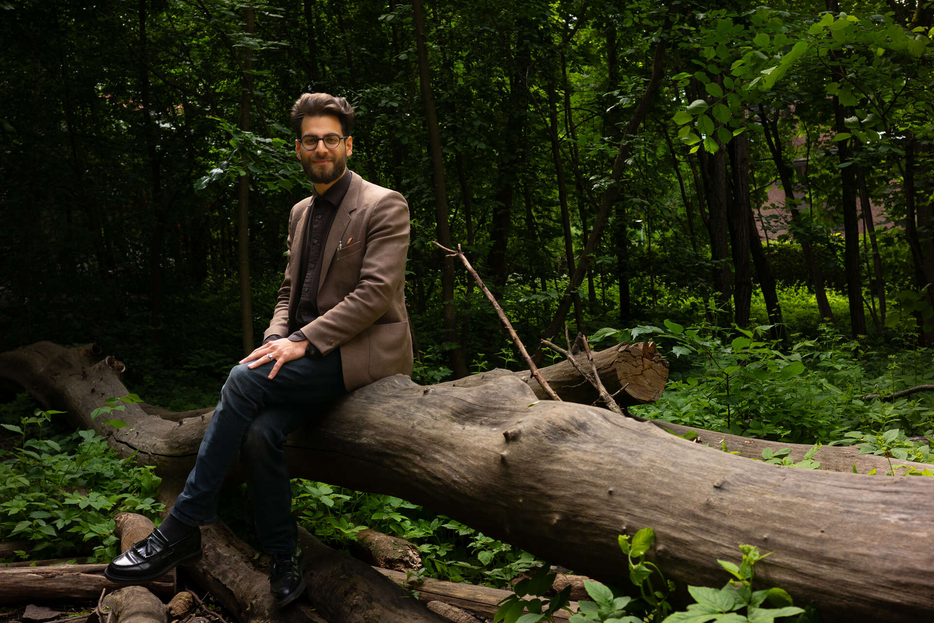 Bilde av Alkazemi i skogen bak Teologisk fakultet i Oslo. Han sitter på en nedfallstamme med løvverk bak eg. 