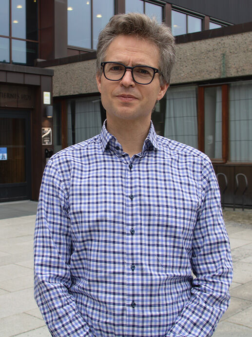 Professor Peder Roberts, en mann med grålig hår og briller, står framfor et bygg med stor glassfasade. 
