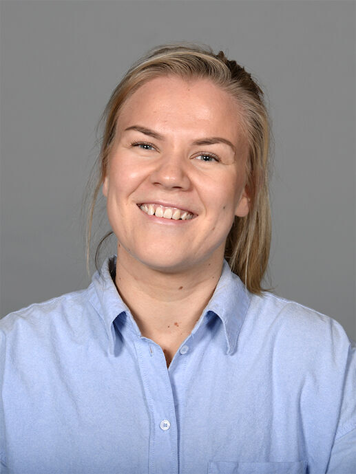 En smilende ung dame lyst hår, blå skjorte og en grå bakgrunn.