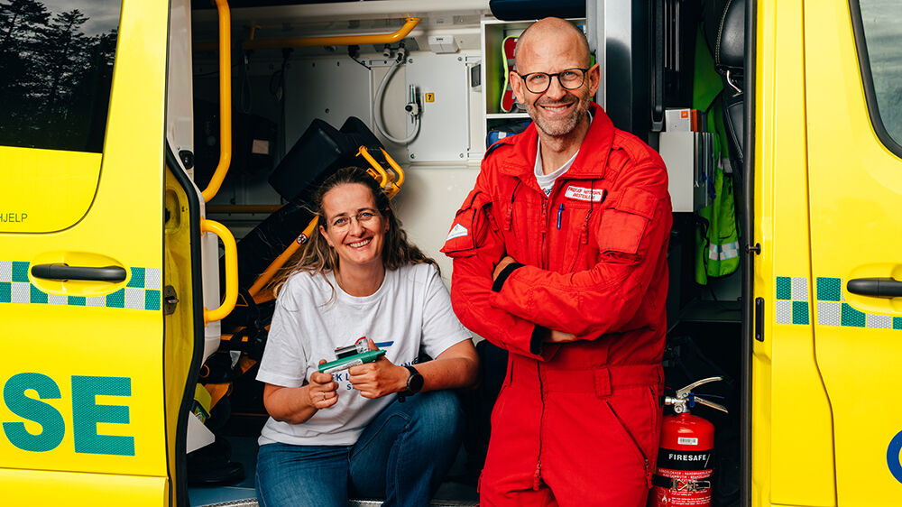 To smilende personer i sidedøren på en ambulansebil. 