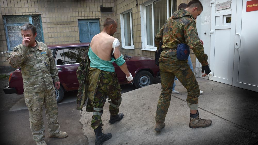 Ukrainske soldater, en såret og en helsepersonell foran klinikk 