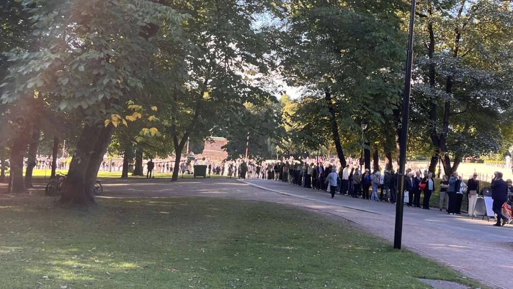 Lang kø av mennesker langs en sti omgitt av grønne trær i Slottsparken.