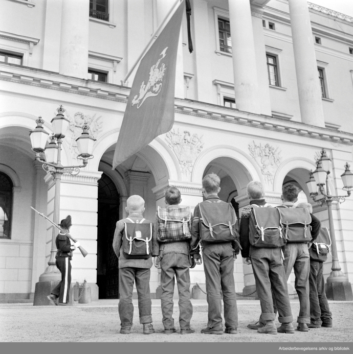 Sort-hvitt foto av seks skolebarn med ryggsekker foran Slottet i Oslo.