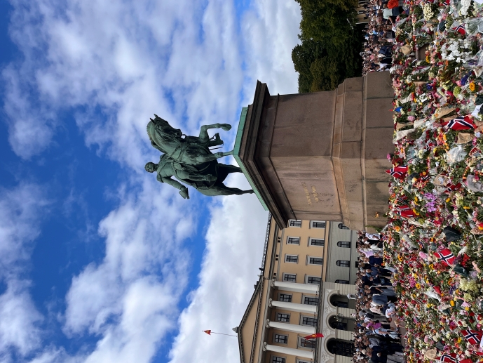 Rytterstatuen av kong Karl III Johan omgitt av et blomsterhav og mennesker på Slottsplassen i Oslo.