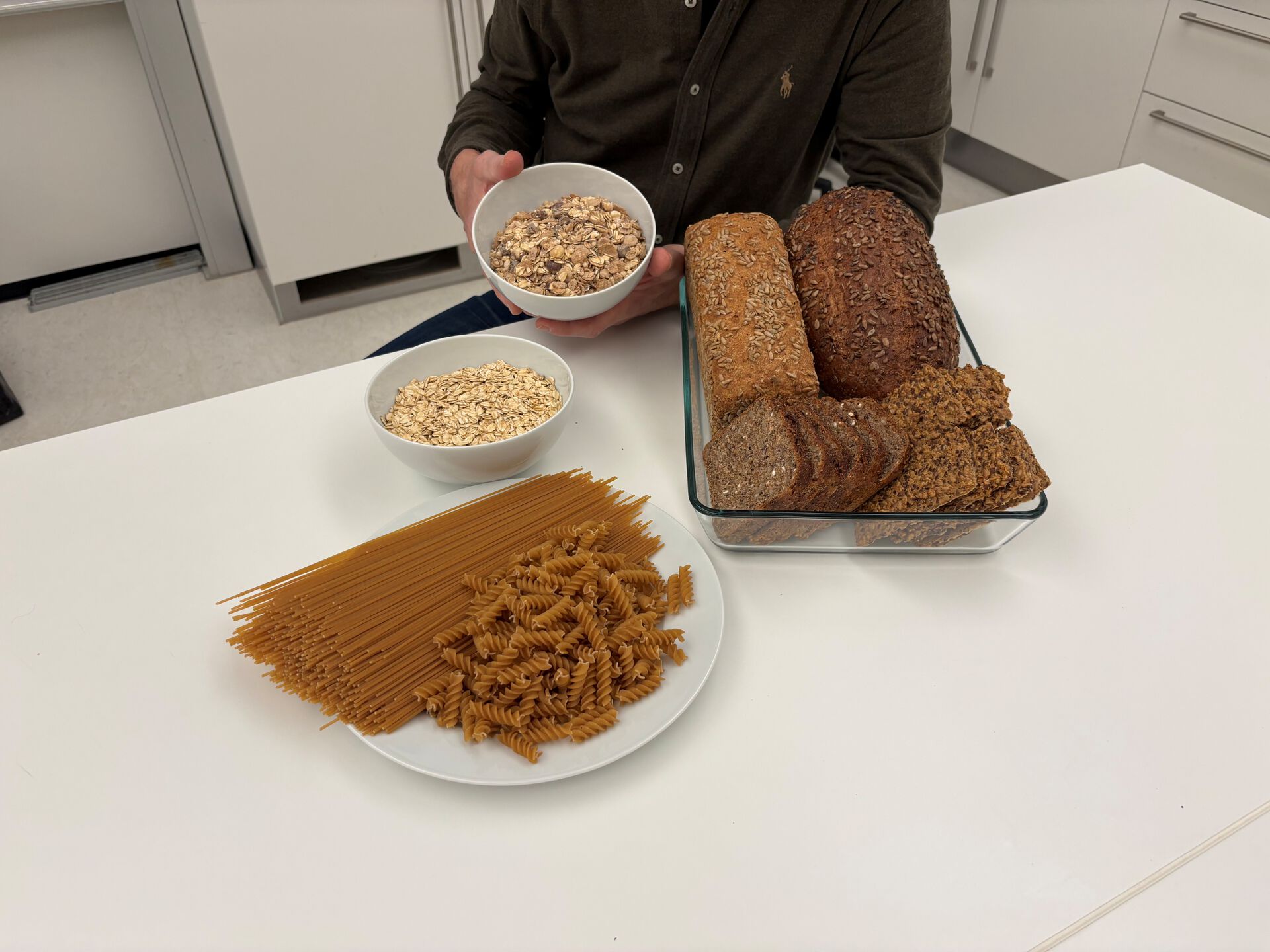 Bildet viser fat med grovt brød, fullkornpasta og frokostblandinger med korn.