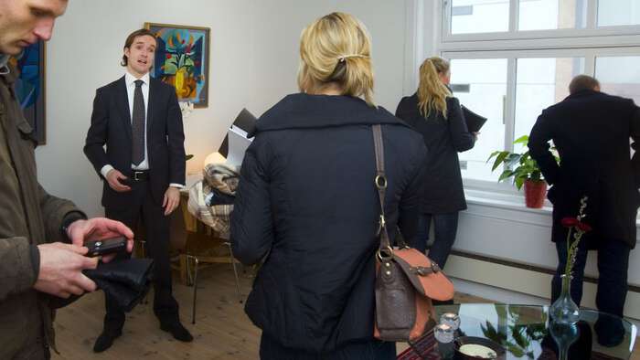 Ung mann med dress og slips viser fram en  leilighet. Mange med ryggen til  ser seg rundt. 