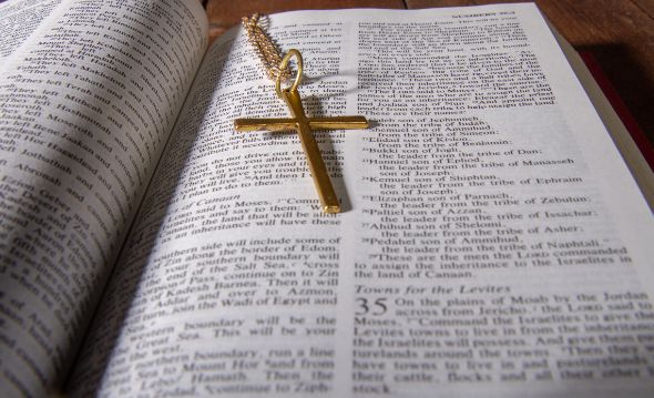 Åpen side i bibelen med et korsanheng.