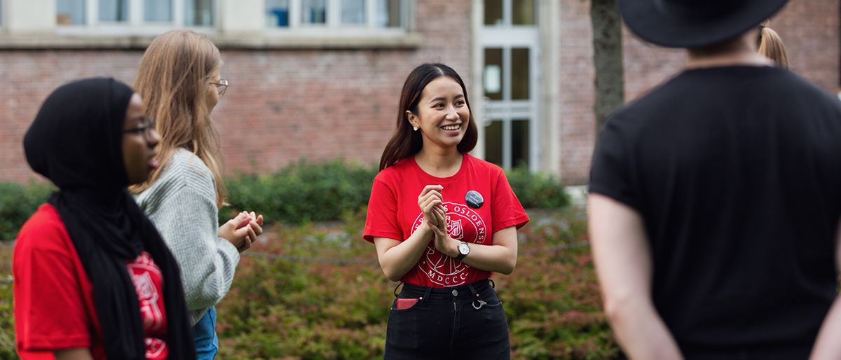 Fire studenter snakker og ler i en gruppe. Tre kvinner og en mann, to av dem er ikledd røde fadderskjorter fra UiO