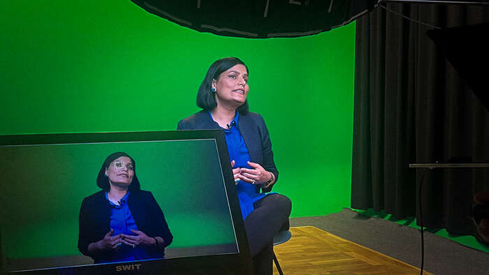 Dr. Gulnaz Anjum in a green screen studio, presenting her script.