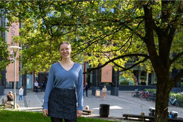 Iris som smiler. Hun står på gress med trær og Georg Sverdrups hus i bakgrunnen. 