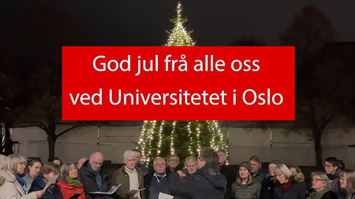 Skjermdump fra film med plakat der det står "God jul fra alle oss ved Universitetet i Oslo" med kor og tent juletre i bakgrunn
