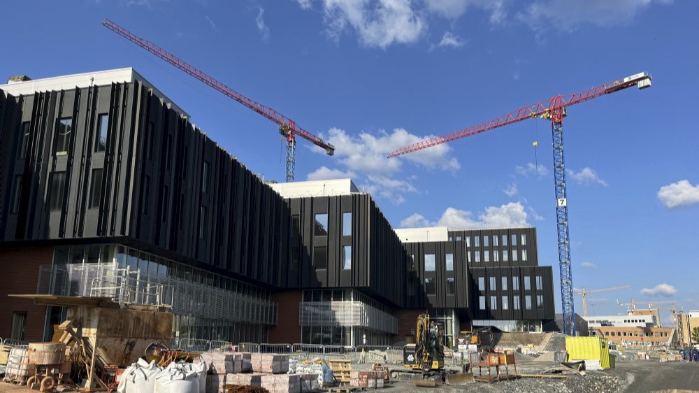 Byggeplassen til Livsvitenskapsbygget, med blå himmel og røde heisekraner i bakgrunnen.