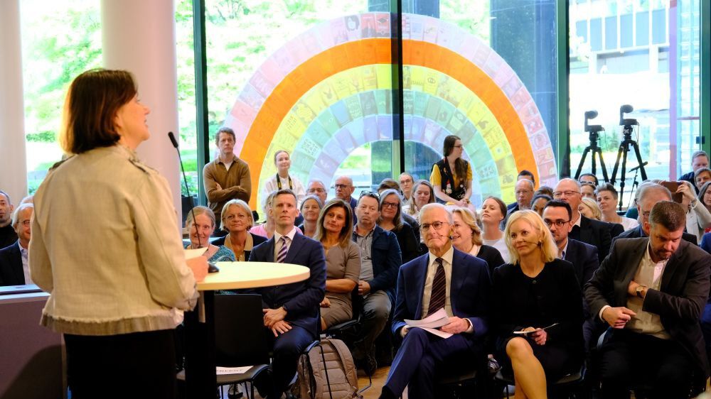 Kvinne står på scene og foran publikum i et bibliotek med blant annet norges statsminister Jonas Gahr Støre.