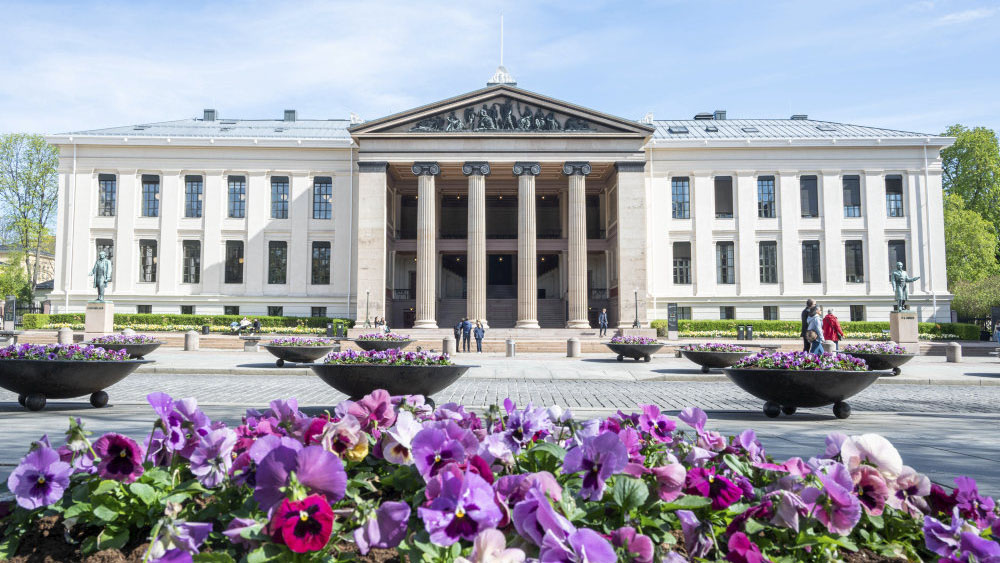 Fasadebilde av Universitetets aula med blomster i forgrunnen