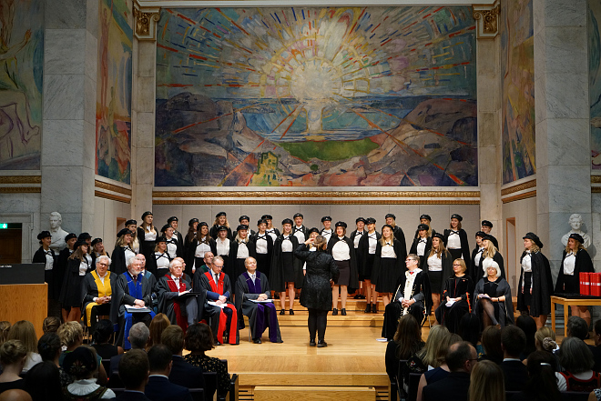 Universitetsledelsen, dekaner og kor på scenen i aulaen. Foto: Terje Heiestad/UiO