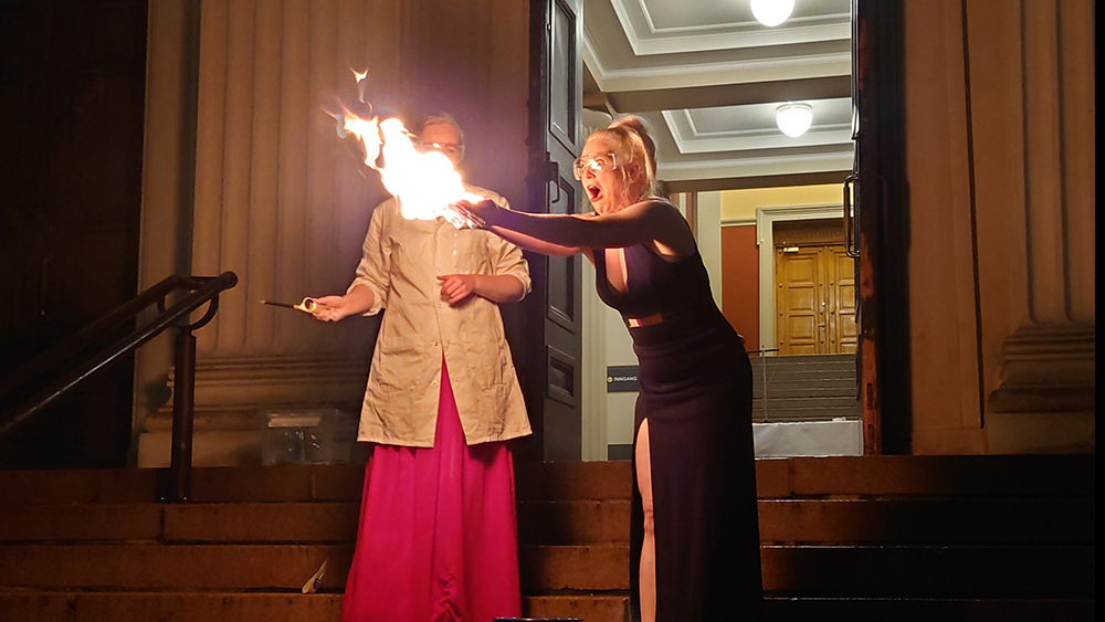 To festkledte studenter med flammer i henende på trappa ved inngangen til Domus Bibliotheca 