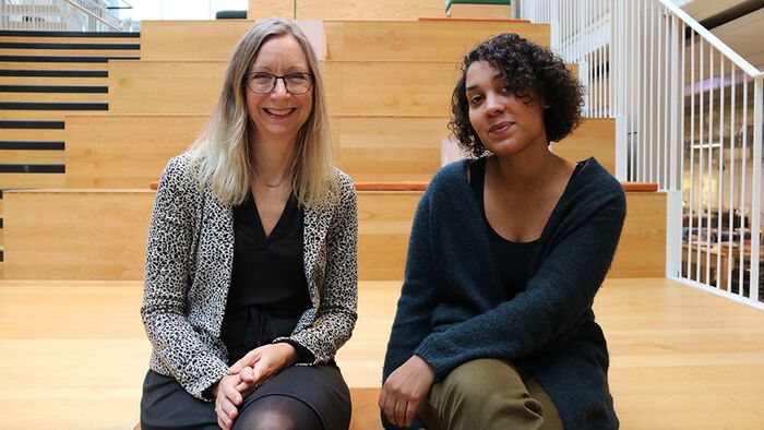 Elisabeth Oxfeldt, lydhudet kvinne med langt blondt hår og briller, og Camara Lundestad Joof, mørkhudet kvinner med mørkebrunt hår, sitter ved siden av hverandre i trapp og smiler.
