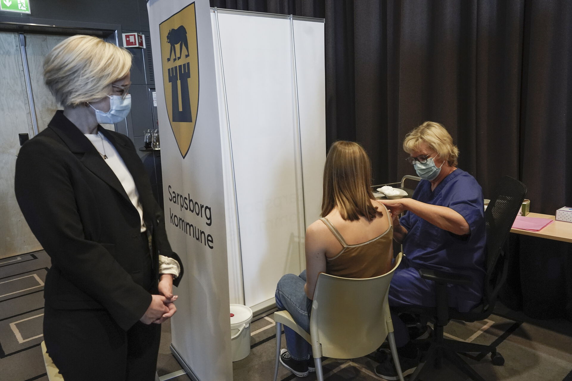 Kvinne med munnbind ser på at helsepersonale setter covid-vaksine i arm på kvinne