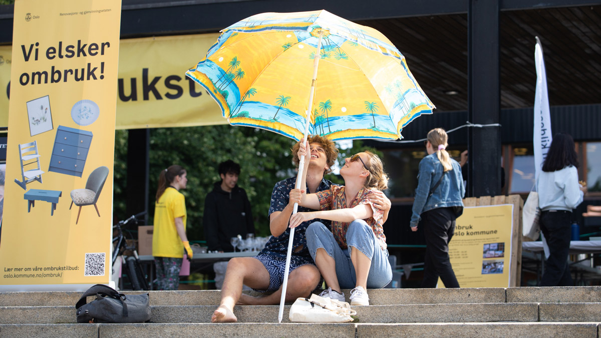 To studenter under en gul parasoll på et torg på Ombruksdagen