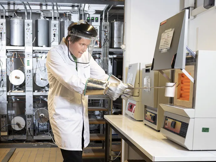 A man wearing a white lab-coat, looking into a big white machine in a lab.