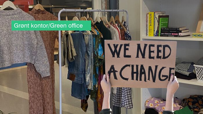 Brukte klær som henger på et stativ ved siden av en bokhylle på Grønt kontor. Inn i bildet er det montert inn hendene til en som holder en plakat med teksten "We need a change". 