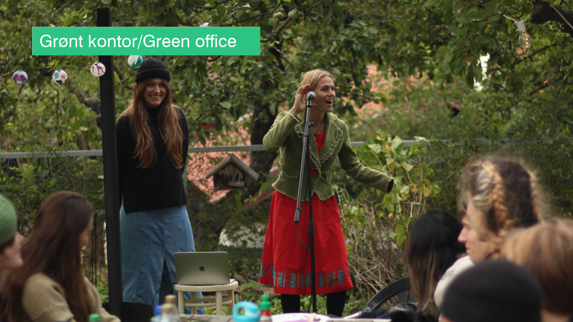 Two young students with a microphone in front of other students in the student garden.