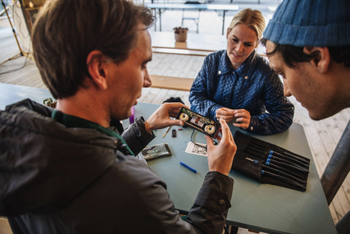 Tre personer som ser på en del til en elektronisk sak. 