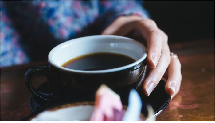 Nærbilde av to hender som holder en sort kopp med kaffe.