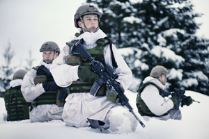 Fire soldater i snølandskap med hvite dresser, grønne hjelmer, skuddsikre vester og hjelmer. 
