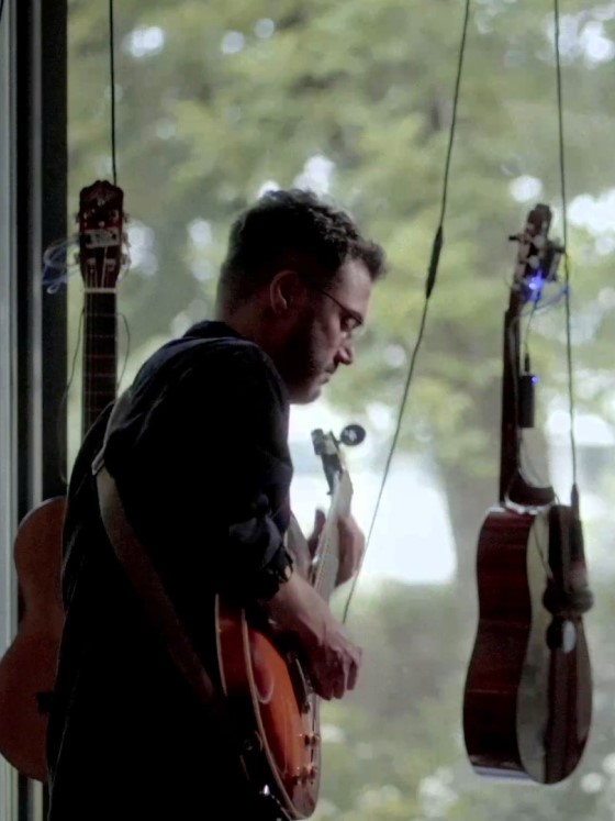 Çağrı Erdem spiller gitar foran to gitarer som henger i luften.