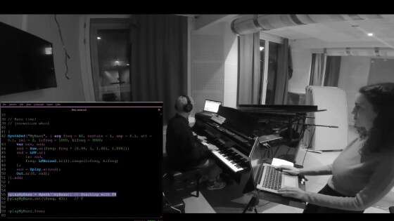 Black and white photo of Anna-Maria standing with a laptop next to a man playing piano.