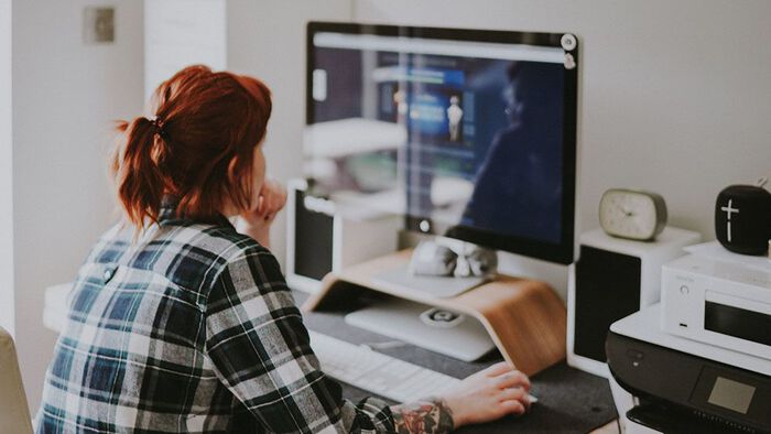 A person sitting by a computer screen in an office. Photo.