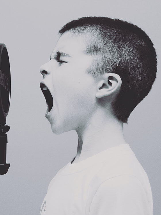 A black and white photo of a boy who screams inside a microphone
