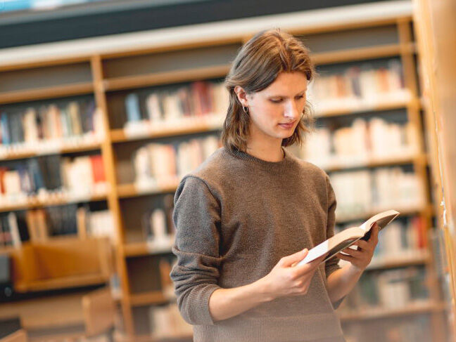 Student sitter i vinduskarm og leser bok